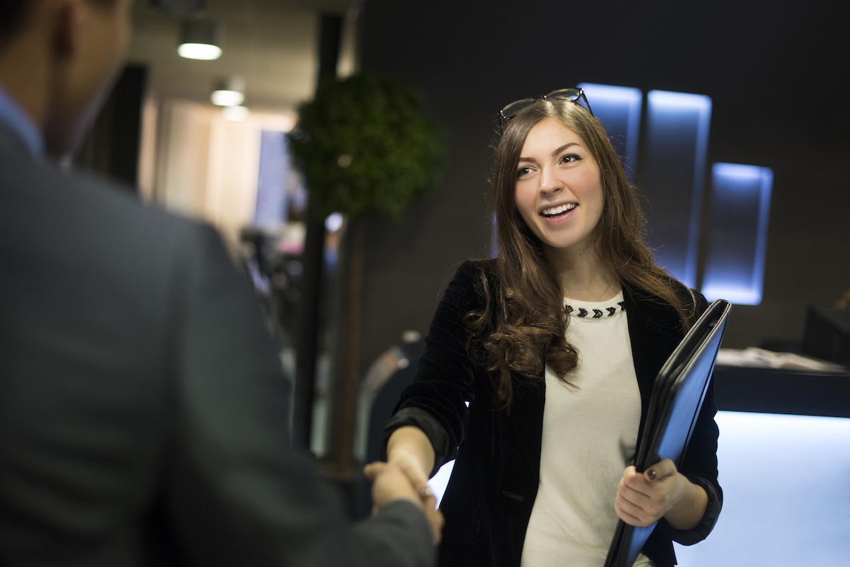 young woman arrives at her interview , resume under her arm greeting her interviewer